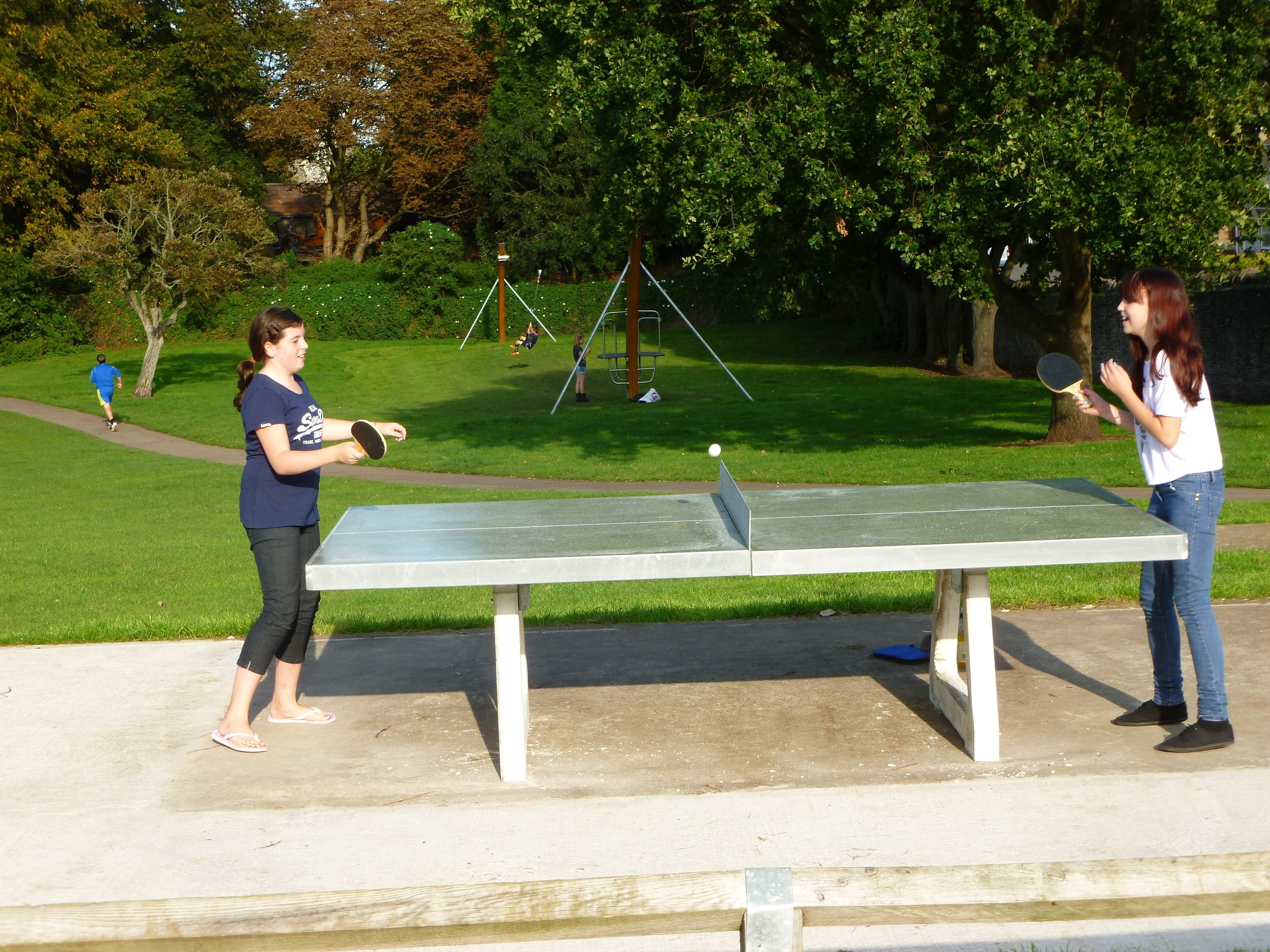 two children playing table tennis on the outdoor table at King George the 5th park