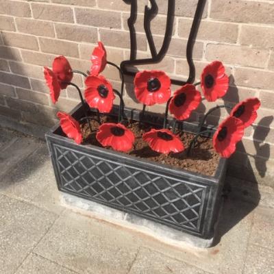 12 red steel poppies in the planter at the base of the Tommy Silhouette