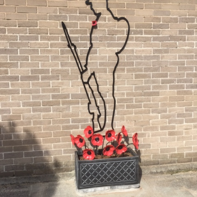 The Six foot There but NotThere Tommy Silhouette with a 12 red steel poppyies in a planter at the base of the Silhouette